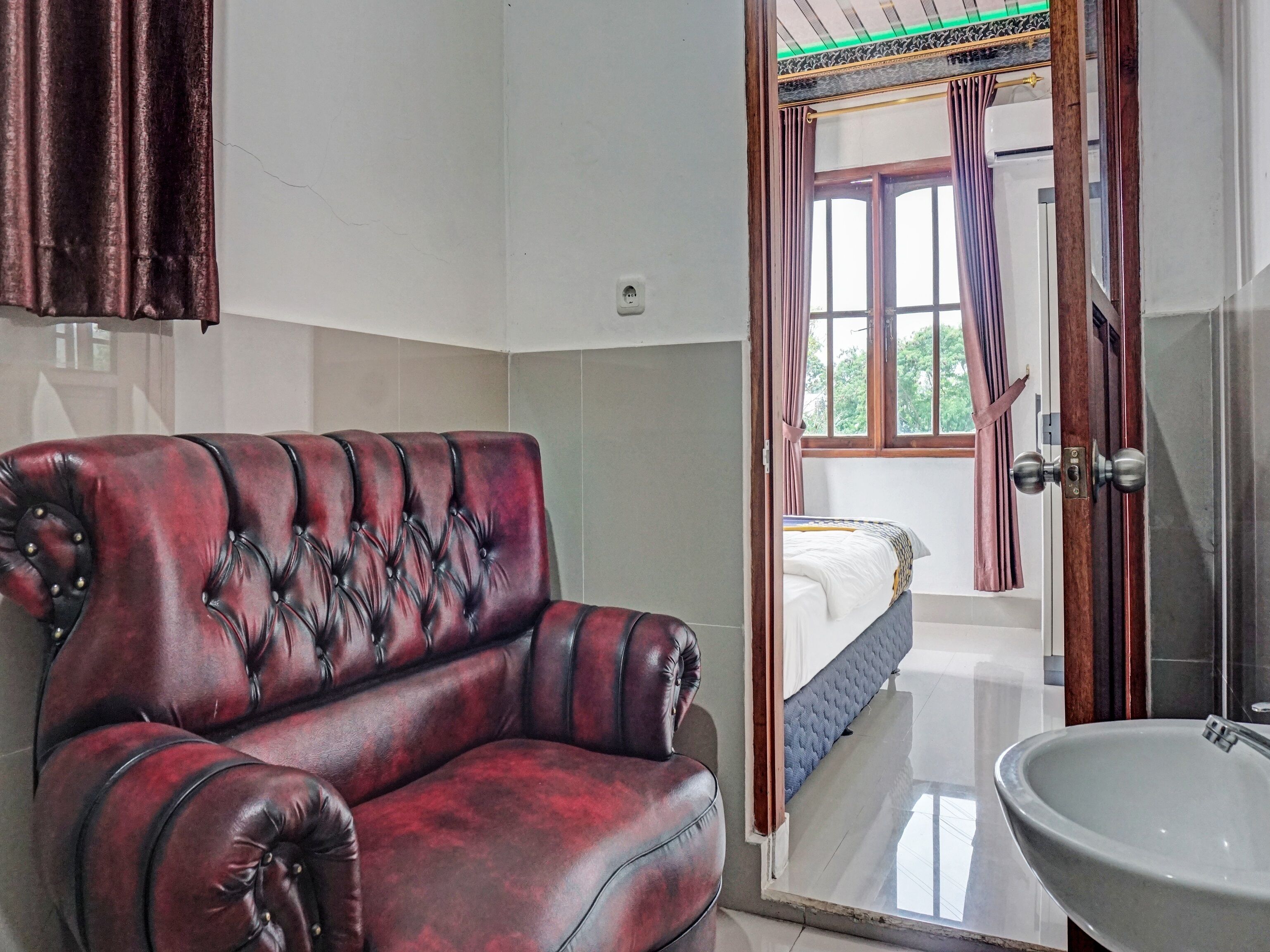 Ein Zimmer mit einem roten Ledersofa, einem großen weißen Waschbecken und einem Fenster mit Vorhängen.