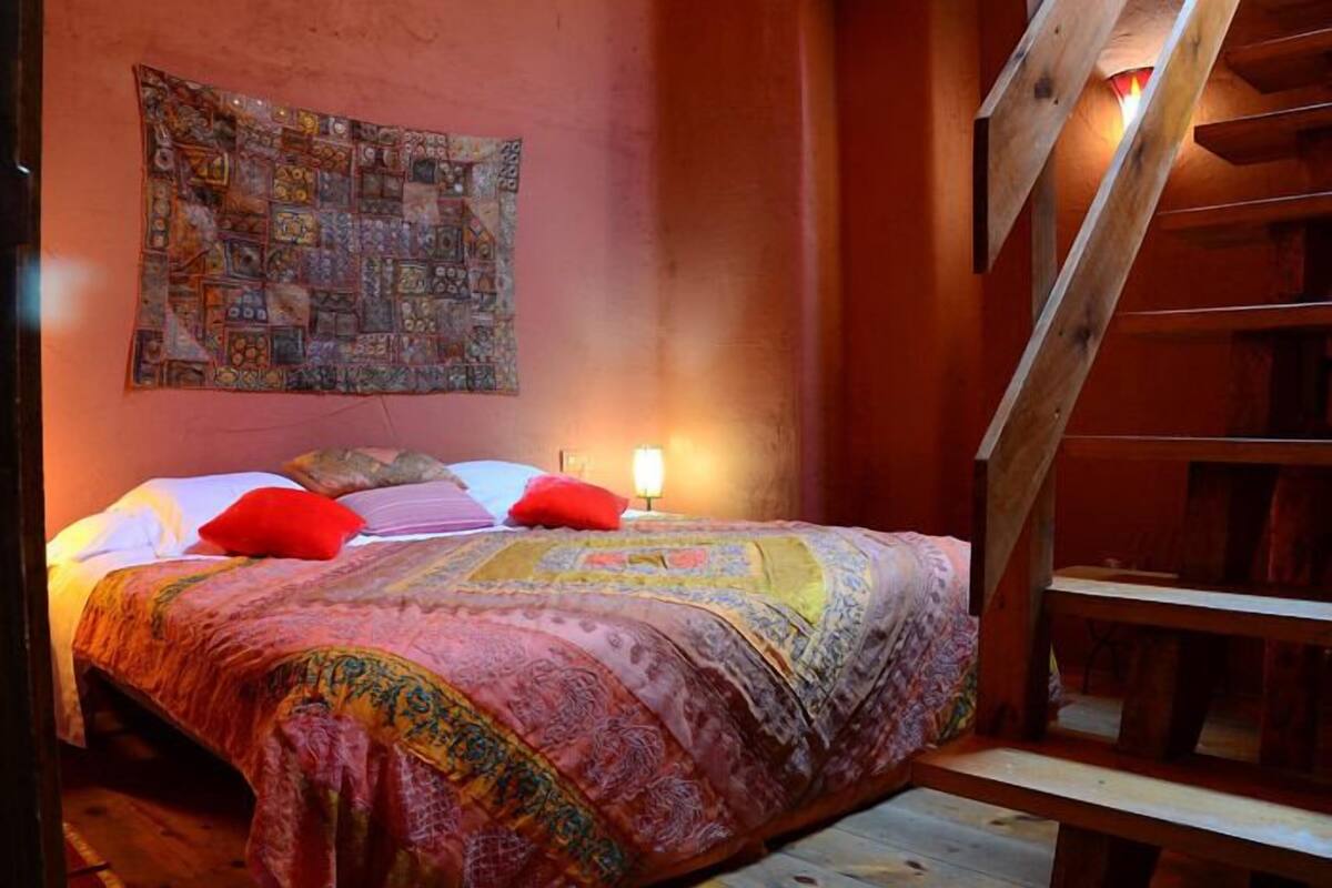 A cozy bedroom with a large bed, a wooden staircase, and a tapestry on the wall.