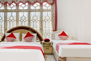 Habitación de hotel con dos camas, cabecero de madera, mesita de noche y ventana con cortinas decorativas.