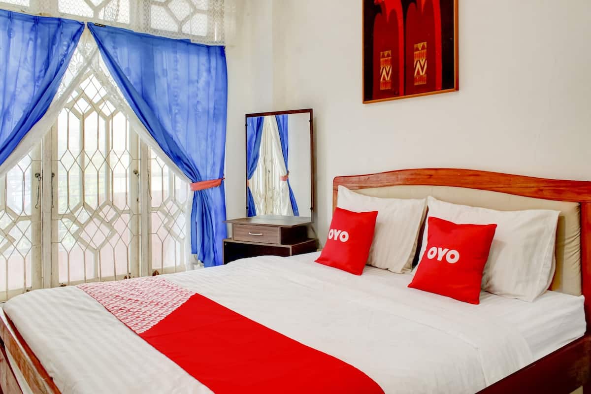 A neatly made bed with white and red bedding, a wooden headboard, and two red pillows with "OYO" text.