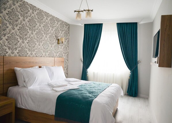 Un lit bien fait, avec du linge de lit blanc et un plaid turquoise, une table de chevet en bois, un papier peint à motifs et une fenêtre ornée de rideaux turquoise.