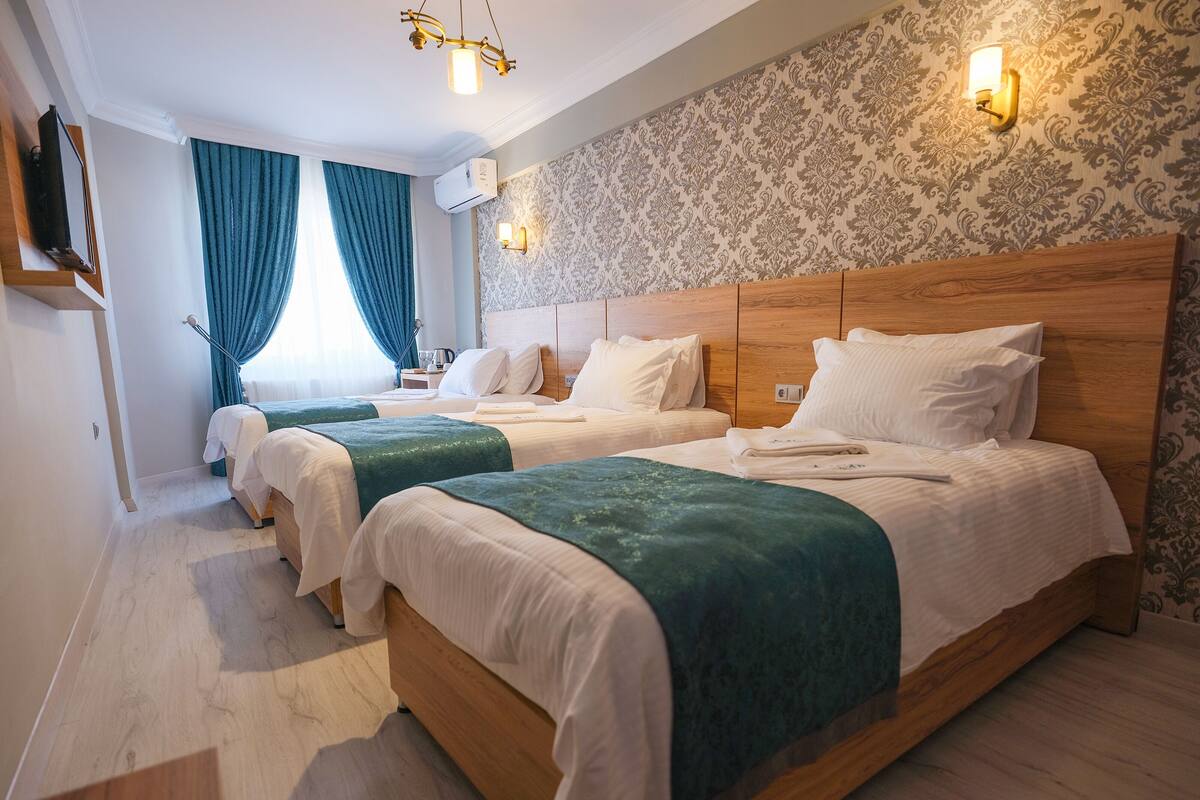 A hotel room with two single beds, a wooden headboard, a wall-mounted TV, and a patterned wallpaper.