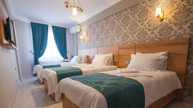 A hotel room with two single beds, a wooden headboard, a wall-mounted TV, and a patterned wallpaper.