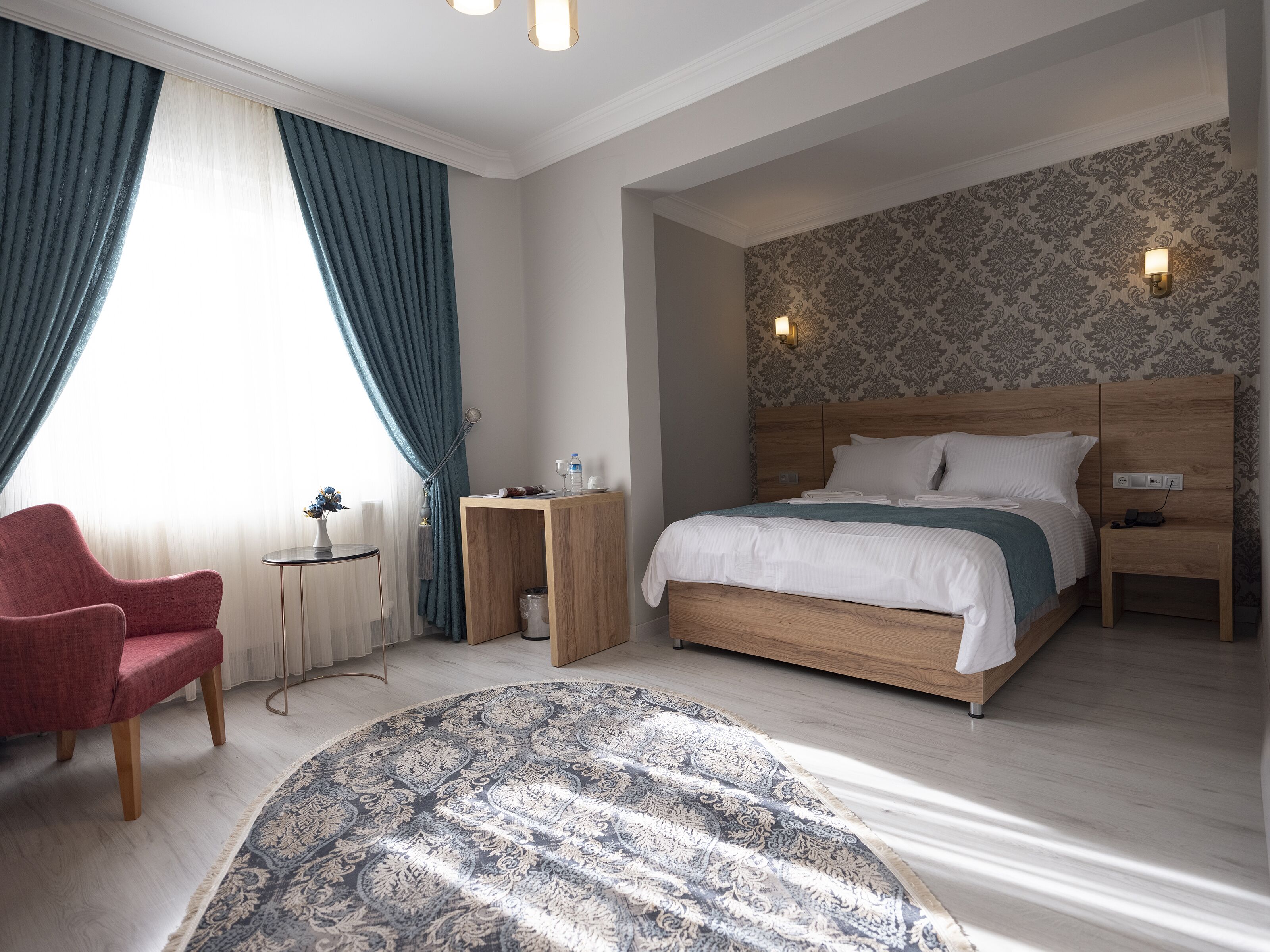 A hotel room with a bed, a chair, a small table, and a patterned rug.