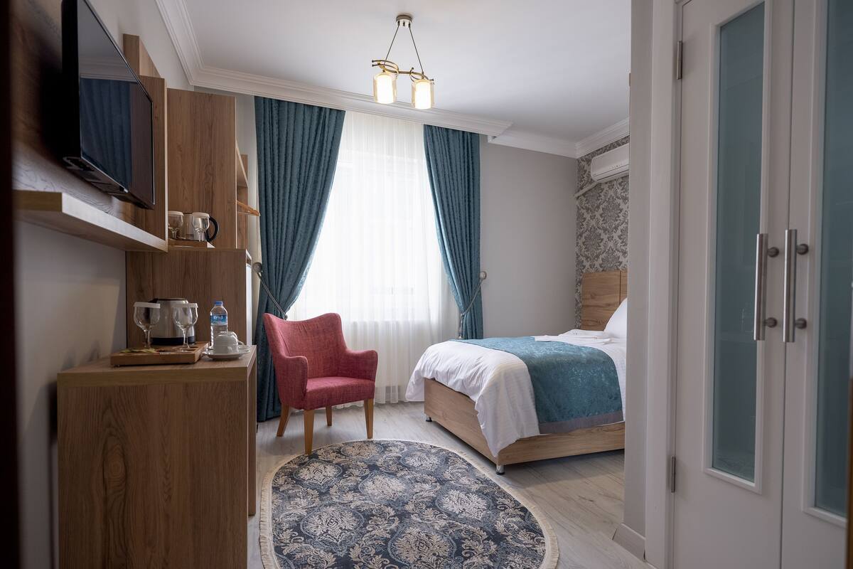 A hotel room with a bed, a desk with a computer, a chair, a TV, and a window with curtains.