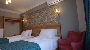 A hotel room with two beds, a wooden headboard, a red chair, and a wall-mounted air conditioner.