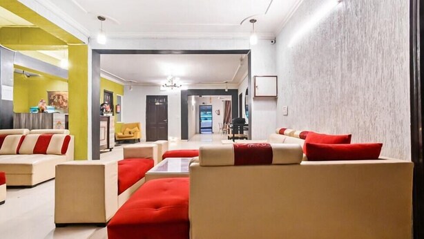 A modern hotel lobby with a neutral color scheme, featuring a reception desk, seating area with sofas and ottomans, and a view into the dining area. - Hello Stay Green (Noida)