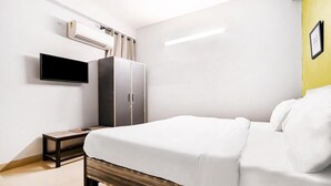 A modern hotel room with a bed, a TV, a wardrobe, and an air conditioning unit. - Hello Stay Green (Noida)
