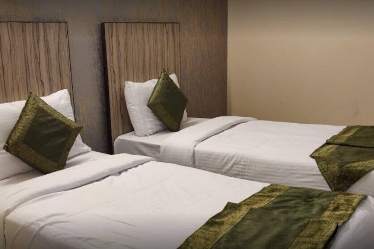 Two single beds with white linens and green throw pillows, wooden headboards, and a beige wall.