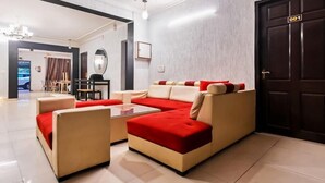 A modern living room with a sectional sofa, a coffee table, and a dining area with chairs. - Hello Stay Green (Noida)