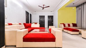 A modern living room with beige sofas and red cushions, a central coffee table, and a ceiling fan. - Hello Stay Green (Noida)