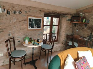 A cozy room with a stone wall, a wooden desk, a green teapot, a framed photo, and a window with a view.
