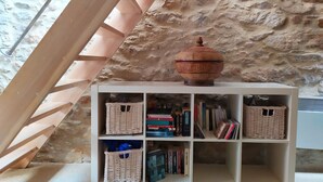 Uma estante com cestos trançados e livros, com o fundo sendo uma parede de pedra e estrutura de madeira.