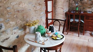 Quarto rústico com parede de pedra, móveis de madeira e uma mesa posta com chaleira, xícaras e um vaso de flores.