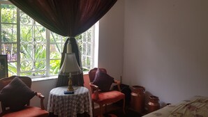 Um quarto com janela, uma mesa com luminária, duas cadeiras e uma cama.