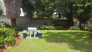 Um jardim bem cuidado com um banco de madeira, diversas plantas e um muro de tijolos.