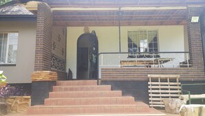 Uma casa com fachada de tijolos, um portão preto e um conjunto de degraus que levam a um alpendre com guarda-corpo.
