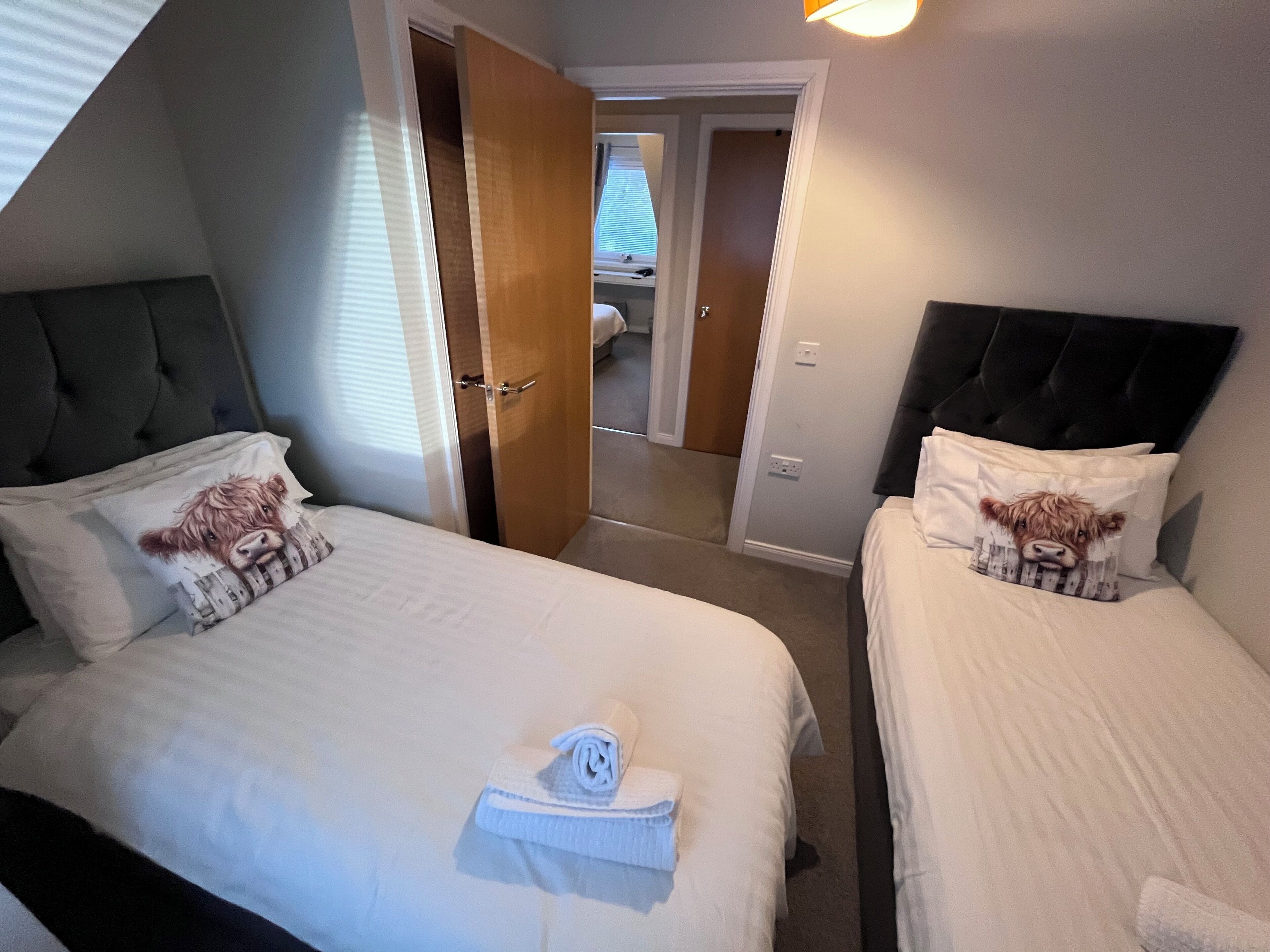 Habitación de hotel con dos camas, cada una con cabecero y almohada con diseño de vaca. Hay una toalla sobre la cama en primer plano.