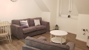Un salon chaleureux avec un canapé gris, une petite table ronde et une chaise blanche.