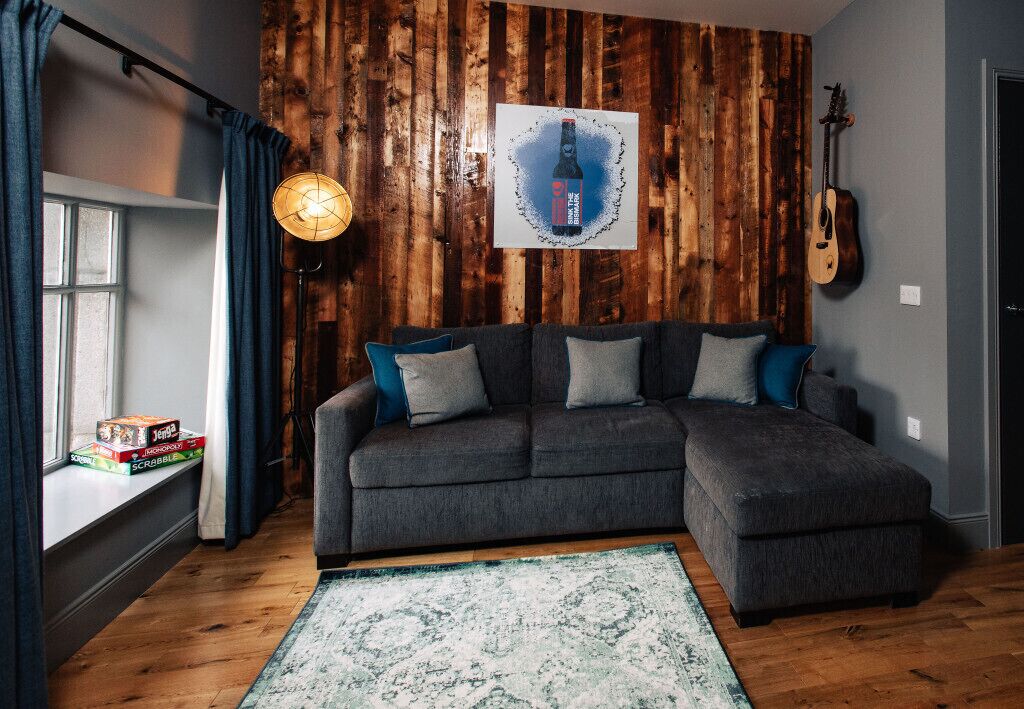 A cozy living room with a sectional sofa, a wooden accent wall, a guitar, and a framed artwork.