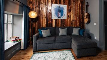 A cozy living room with a sectional sofa, a wooden accent wall, a guitar, and a framed artwork.