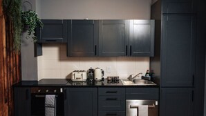 A modern kitchen with dark cabinets, a stainless steel sink, and a built-in oven. - Brewdog Kennels Aberdeen (Aberdeen)