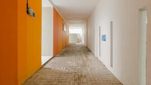A hallway with a brick floor, white walls, and orange accents. There is a sign on the right wall and a door at the end. - OYO 2228 Arwinda Costel (Cianjur)