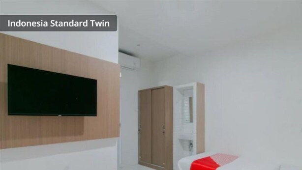 A standard twin room with a TV, wardrobe, and a bed with a red and white patterned bedspread. - OYO 2228 Arwinda Costel (Cianjur)