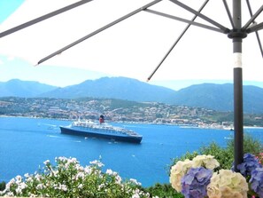 Ein großes Kreuzfahrtschiff auf ruhiger See, im Hintergrund Stadtansicht und Berge.