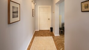 Un couloir doté d’un parquet en bois disposé en motif à chevrons, une porte blanche au fond et des tableaux encadrés accrochés aux murs.