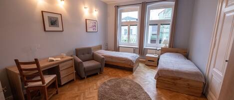 A bedroom with a desk, two single beds, a chair, and a round rug.