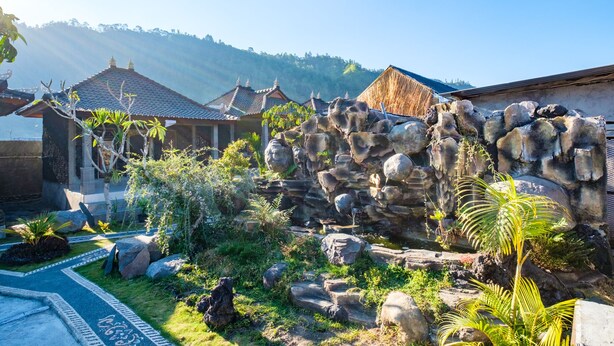 A traditional courtyard with stone walls, potted plants, and a pathway leading to a building with a tiled roof. - Latengaya Mount Batur Bungalow (Kintamani)