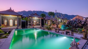 A serene pool area with a stone building, a thatched-roof structure, and a statue. - Latengaya Mount Batur Bungalow (Kintamani)
