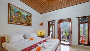 A hotel room with a large bed, a painting on the wall, and a view of the garden through the door. - Latengaya Mount Batur Bungalow (Kintamani)