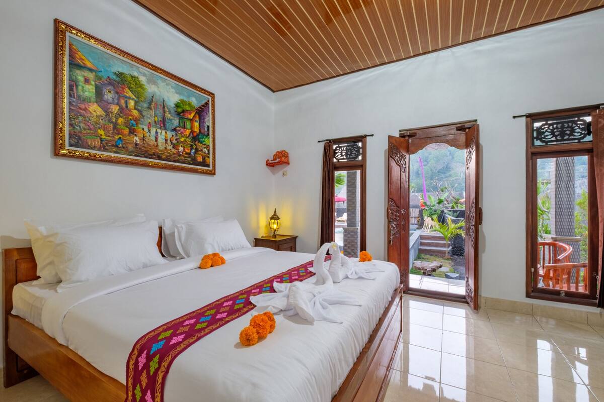 Un cuarto de hotel con una cama grande, un cuadro en la pared y vistas del jardín a través de la puerta.