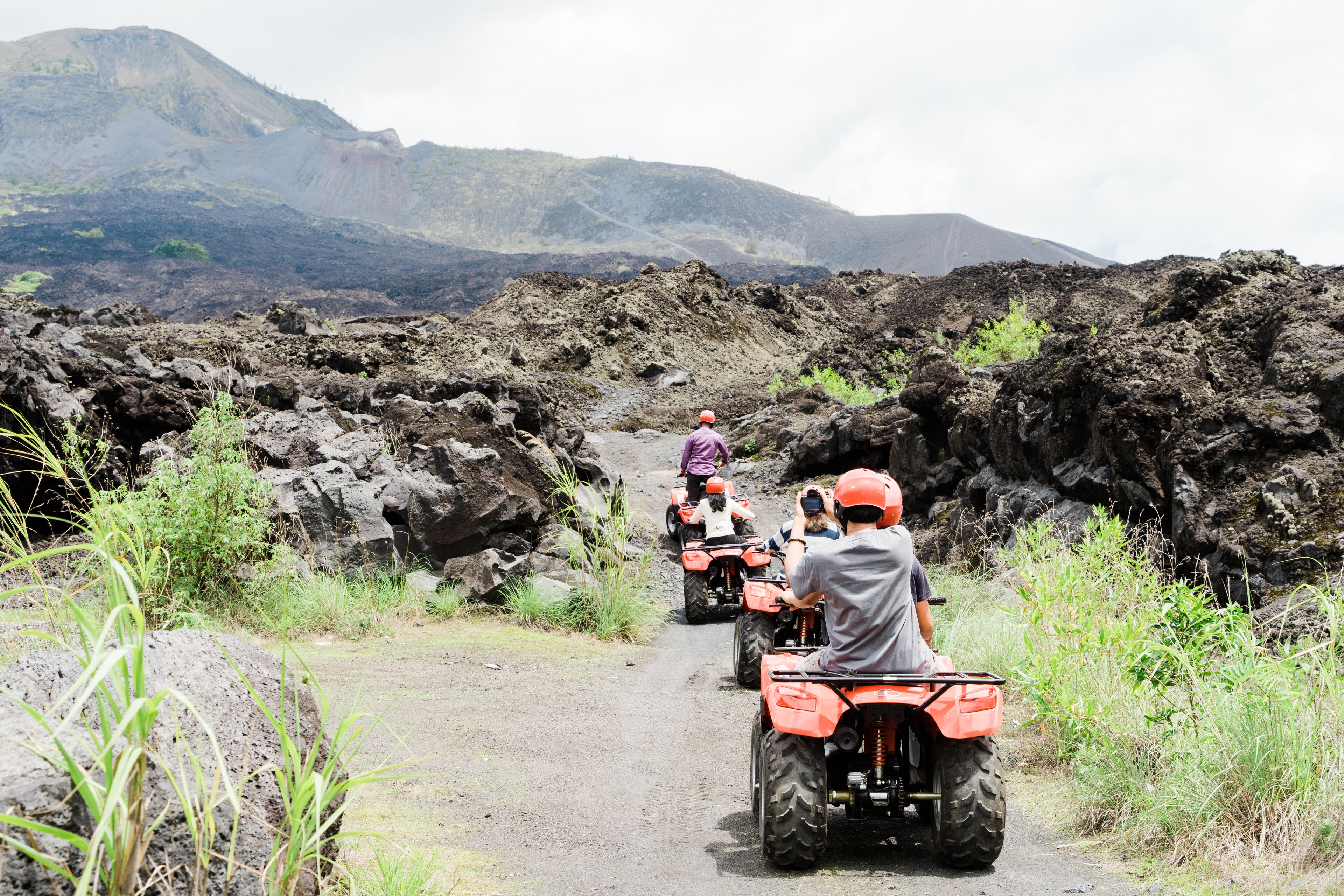 A group of people on ATVs on a rocky path with mountains in the background.