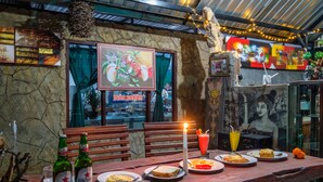 A wooden table with plates of food, a candle, and bottles of Bintang beer. - Latengaya Mount Batur Bungalow (Kintamani)