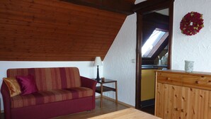 A cozy room with a wooden ceiling, a red sofa with patterned cushions, a small table with a lamp, and a wooden cabinet. - Cozy, homely apartment (Lindau-Bodolz)