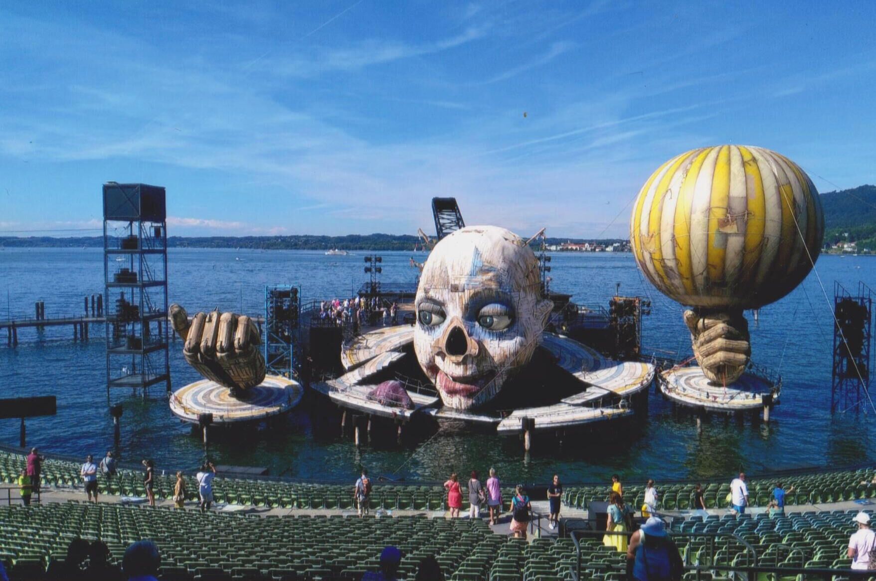 Escultura grande ao ar livre com um crânio e um globo, cercada por água e um cais.