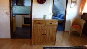 A room with a wooden cabinet, a wicker chair, and a bed with blue pillows. - Cozy, homely apartment (Lindau-Bodolz)