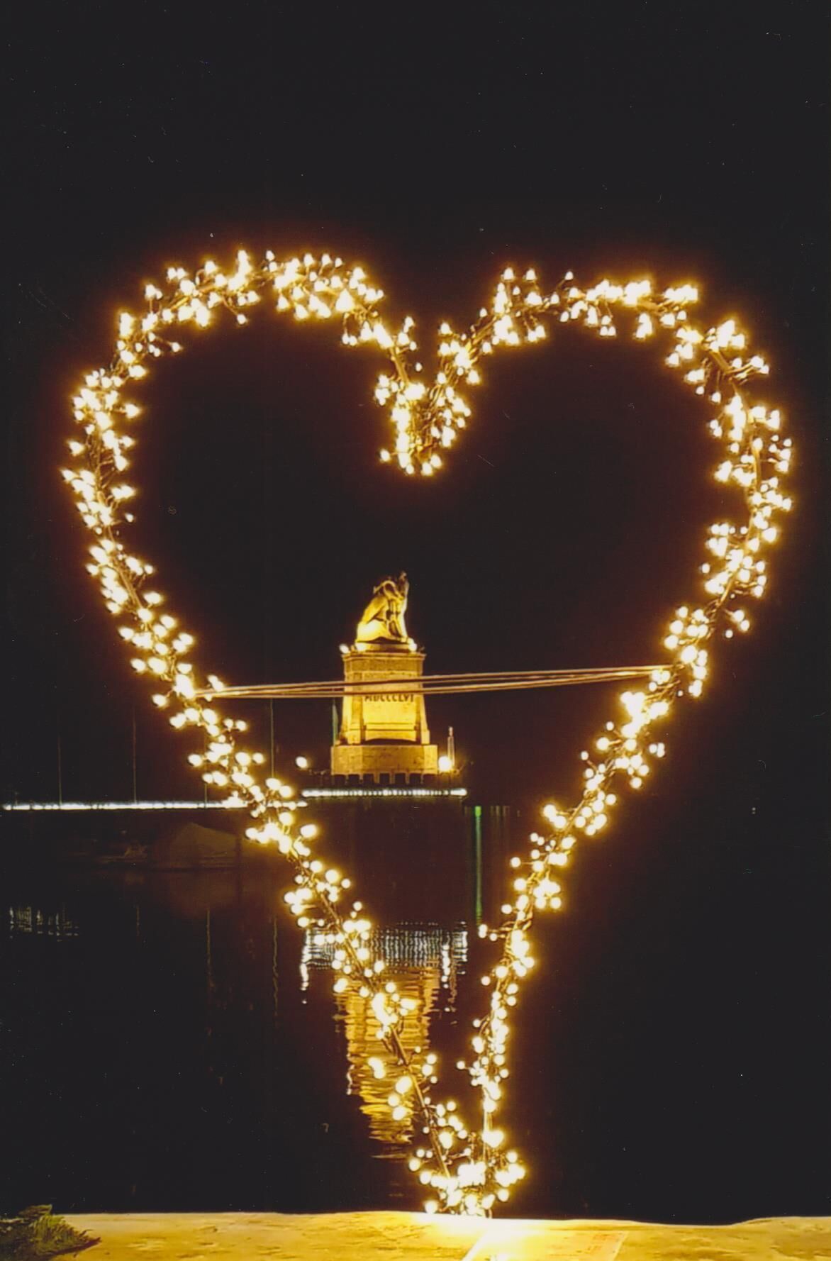 Un jeu de lumière en forme de cœur dans le ciel nocturne, avec un bâtiment en arrière-plan.