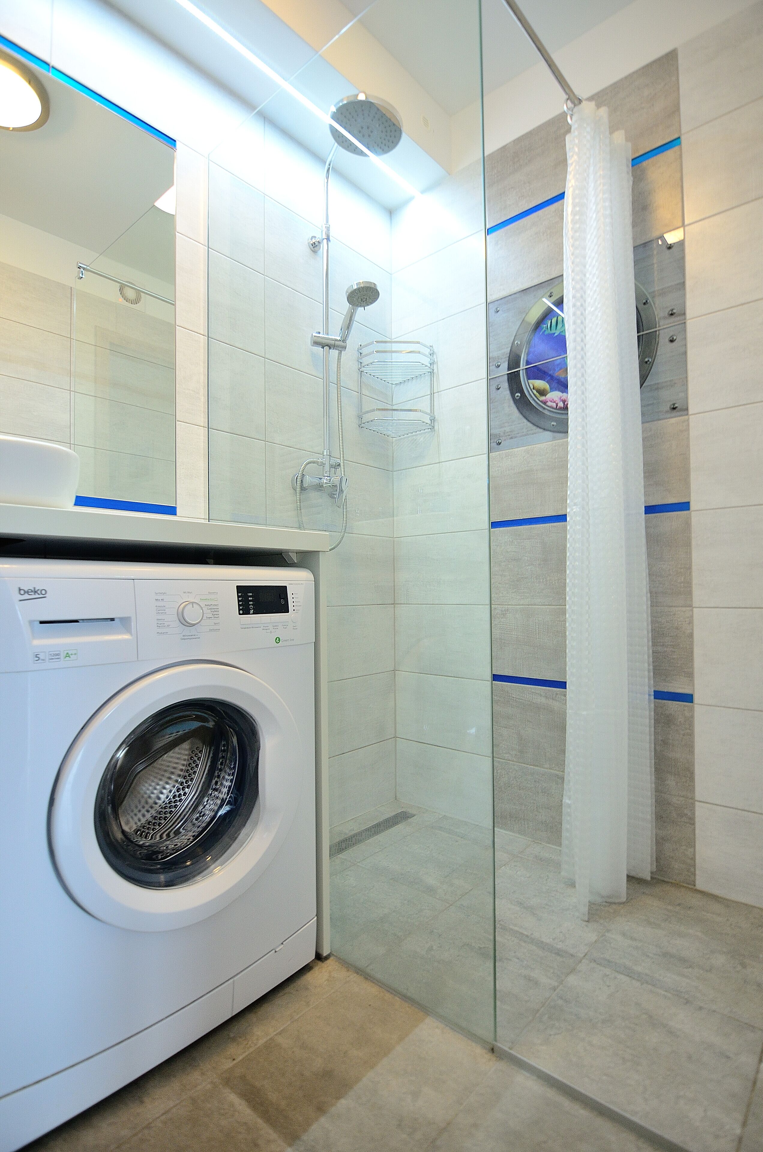 A modern bathroom with a glass-enclosed shower, a built-in washing machine, and a tiled floor.