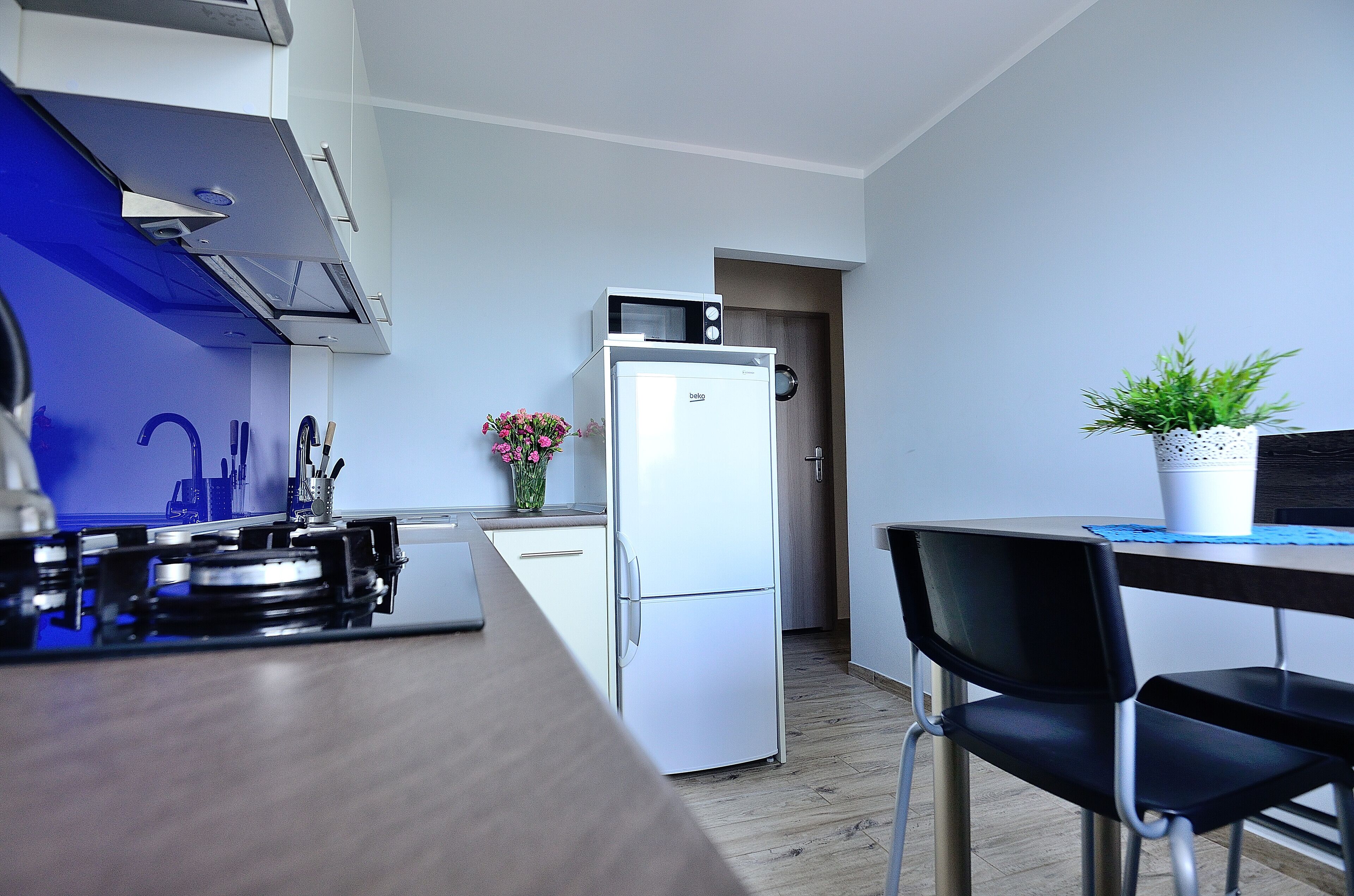 A modern kitchen with a built-in stove, a white refrigerator, and a dining area with a table and chairs.