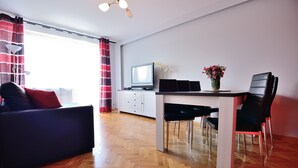 A modern living room with a sofa, a dining table with chairs, a TV, and a vase with flowers. - Victus Apartmenty - Jantar (Sopot)
