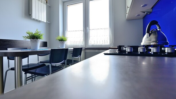 A modern kitchen with a long countertop, two chairs, a potted plant, and a kettle. - Victus Apartmenty - Jantar (Sopot)