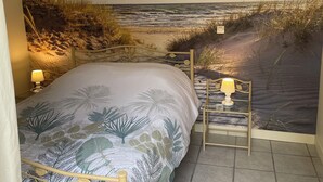 Una camera da letto con un murale raffigurante una spiaggia, un letto con copripiumino a tema tropicale e due comodini con lampade.