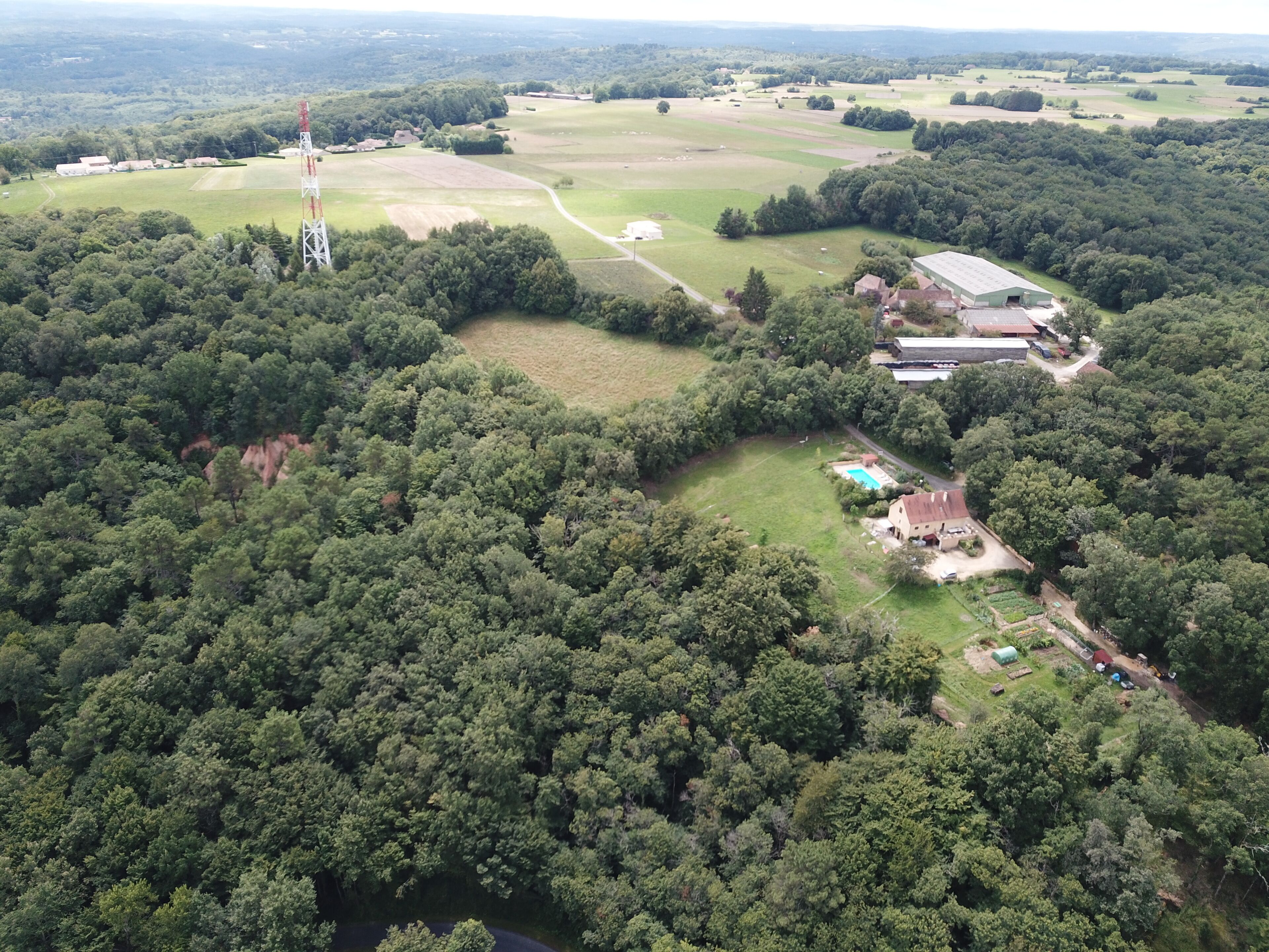 An aerial view of a rural property with a large field, a swimming pool, and a building with a sloped roof.
