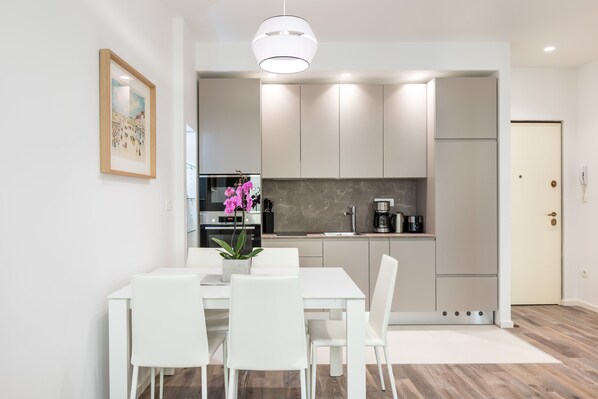 A modern kitchen with white cabinets, a built-in oven, and a coffee machine.