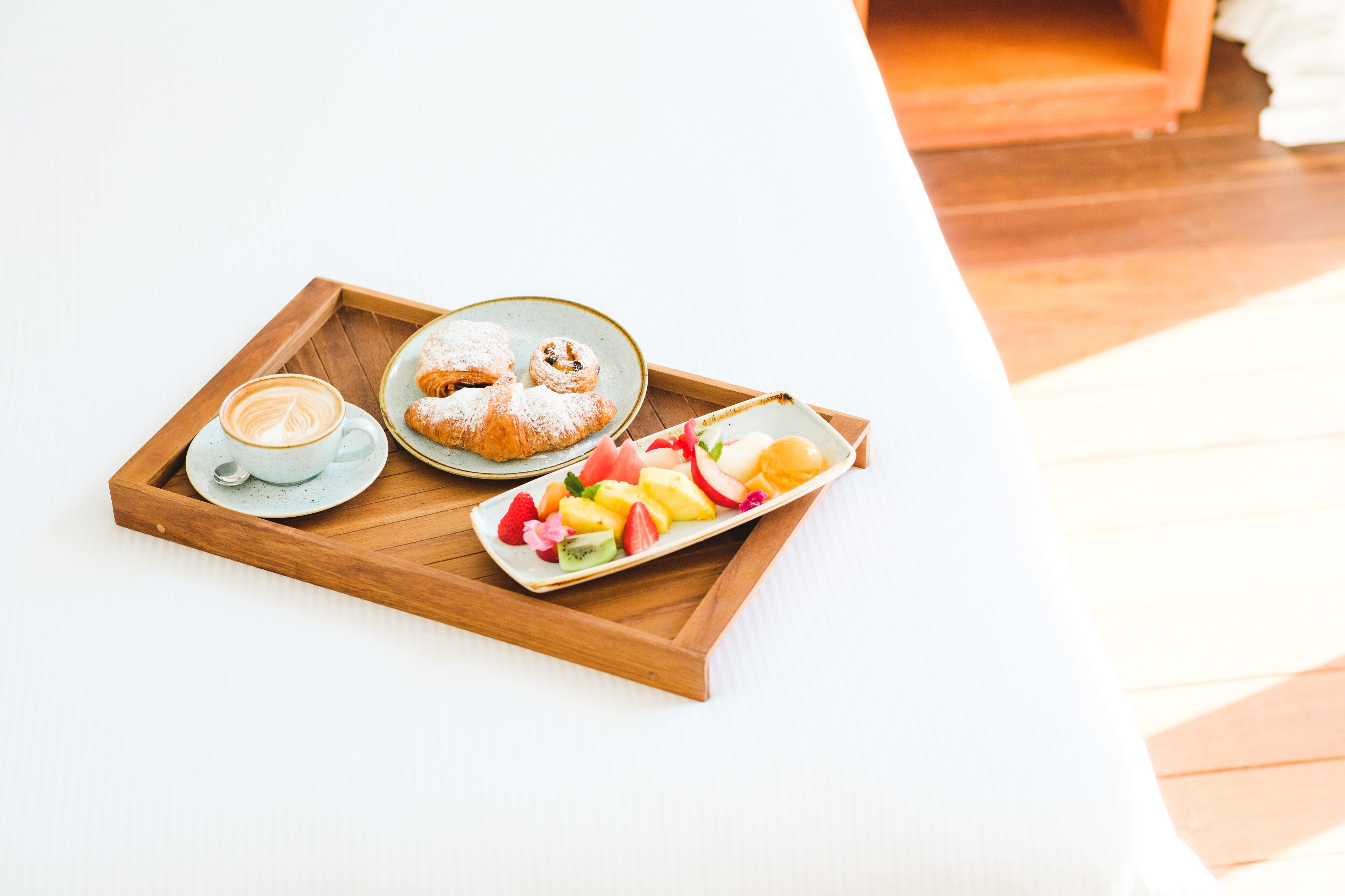 A tray with a cup of coffee, a pastry, and a plate of fruit on a white table.