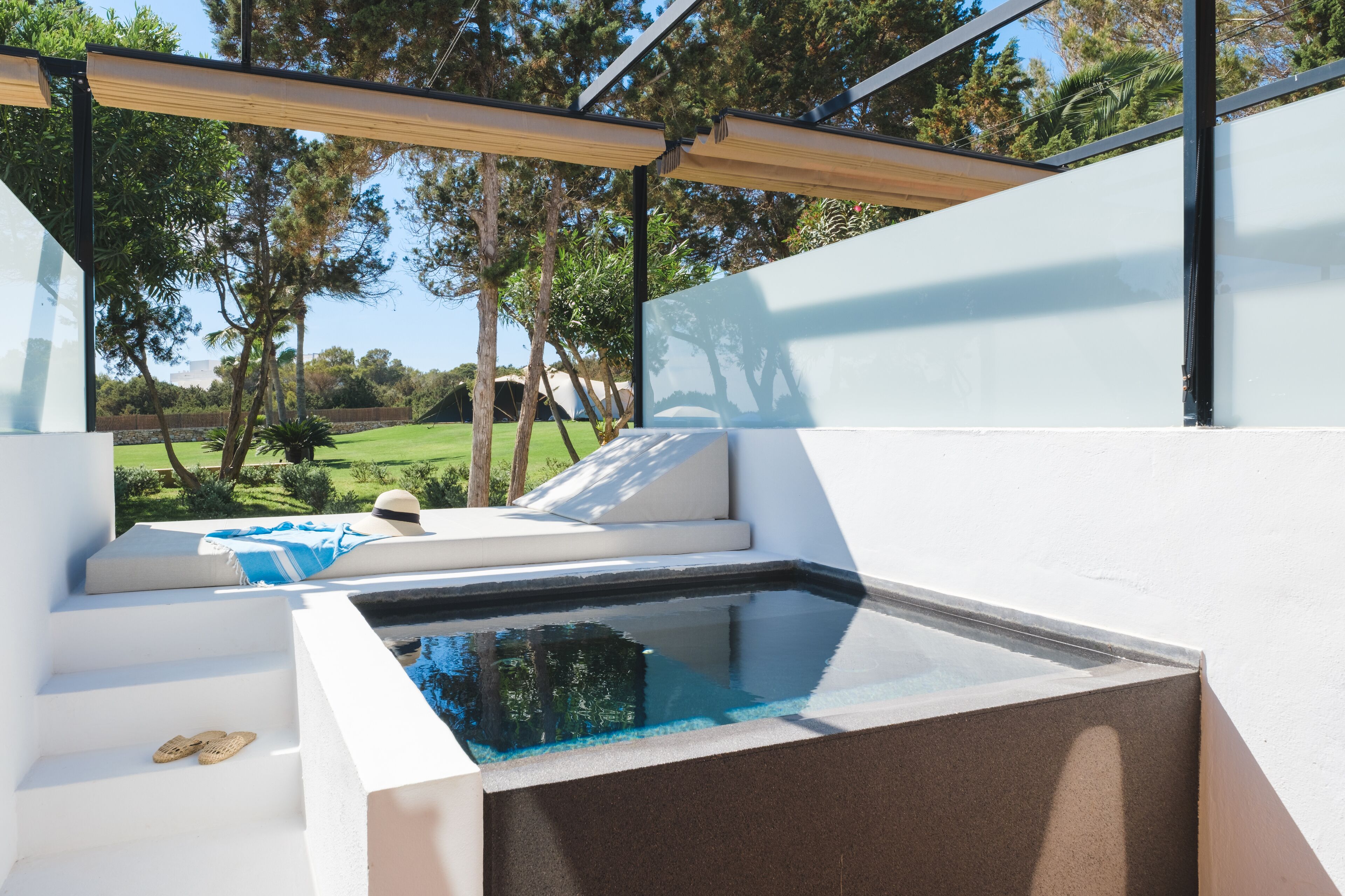 Un área de piscina moderna al aire libre con una zona de estar integrada, rodeada por un muro blanco y una pérgola de madera.